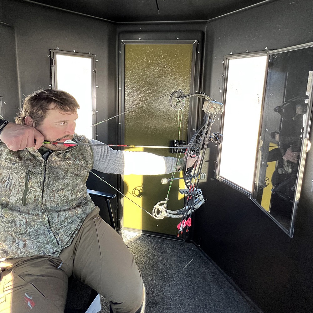 Man drawing bow in hunting blind